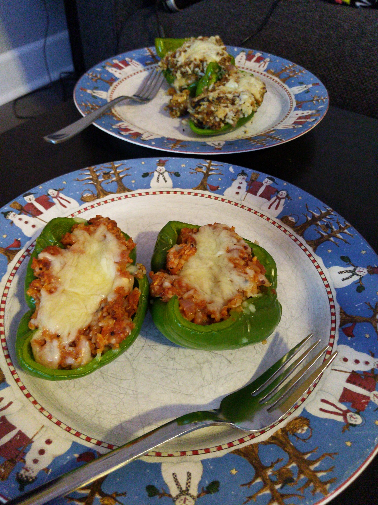 2 plates of Bell peppers halves filled with stuff and covered in cheese.
