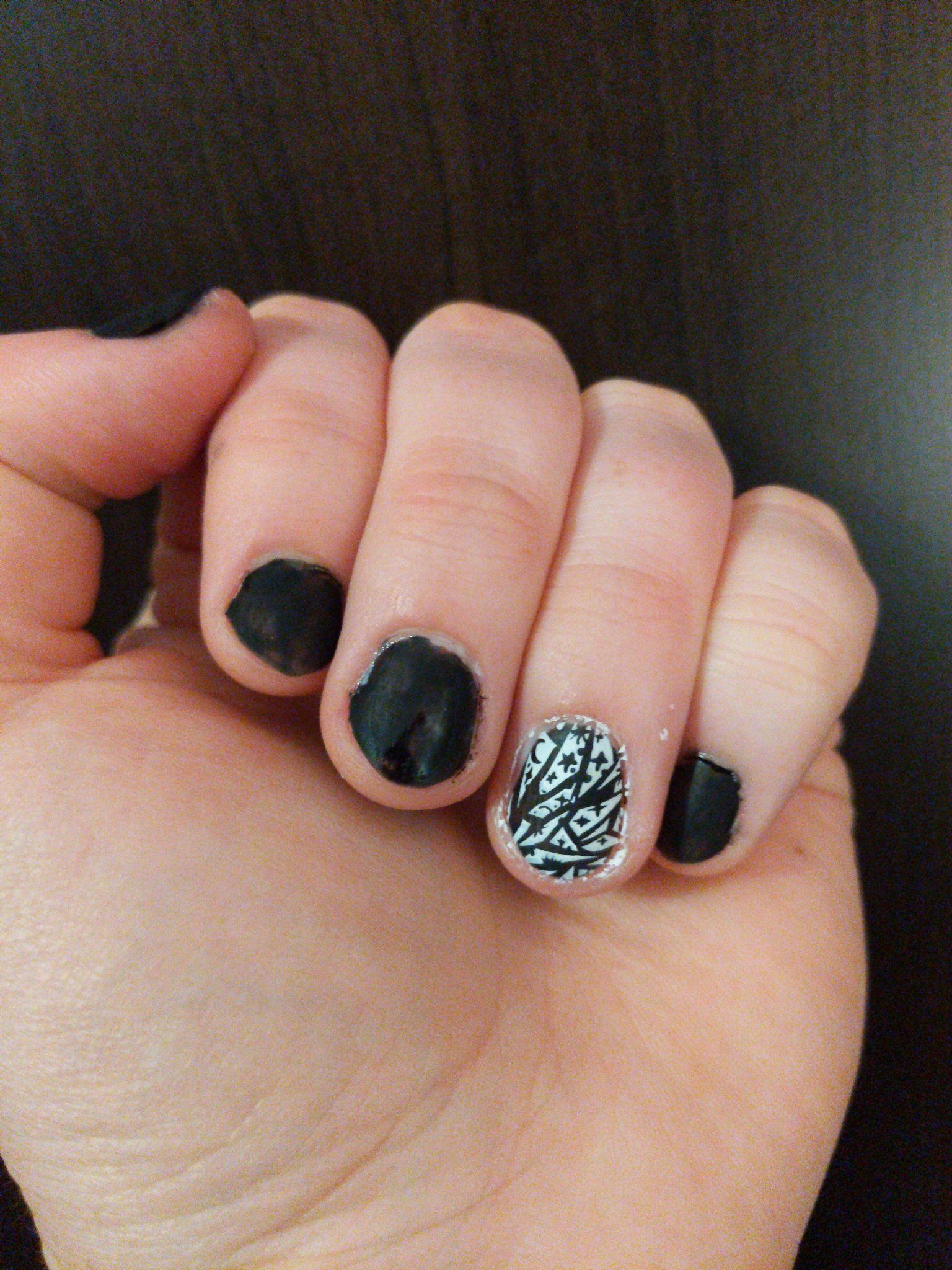 my left hand with matte black nail polish. the ring finger has a black and white pattern of outer space and pieces of shattered glass.