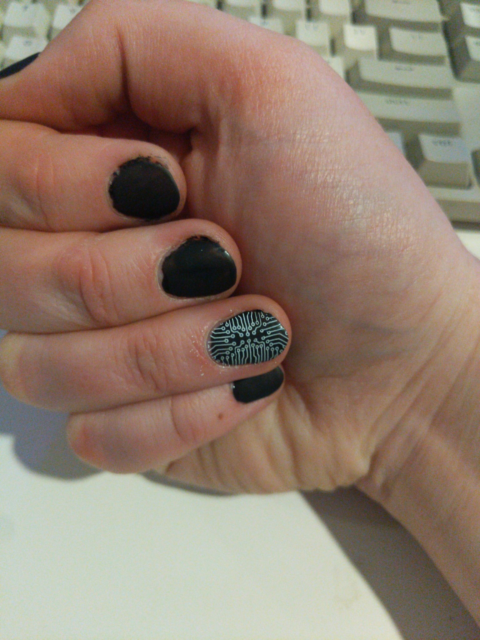 my hand with matte black nail polish. the ring finger has a black and white circuit pattern.
