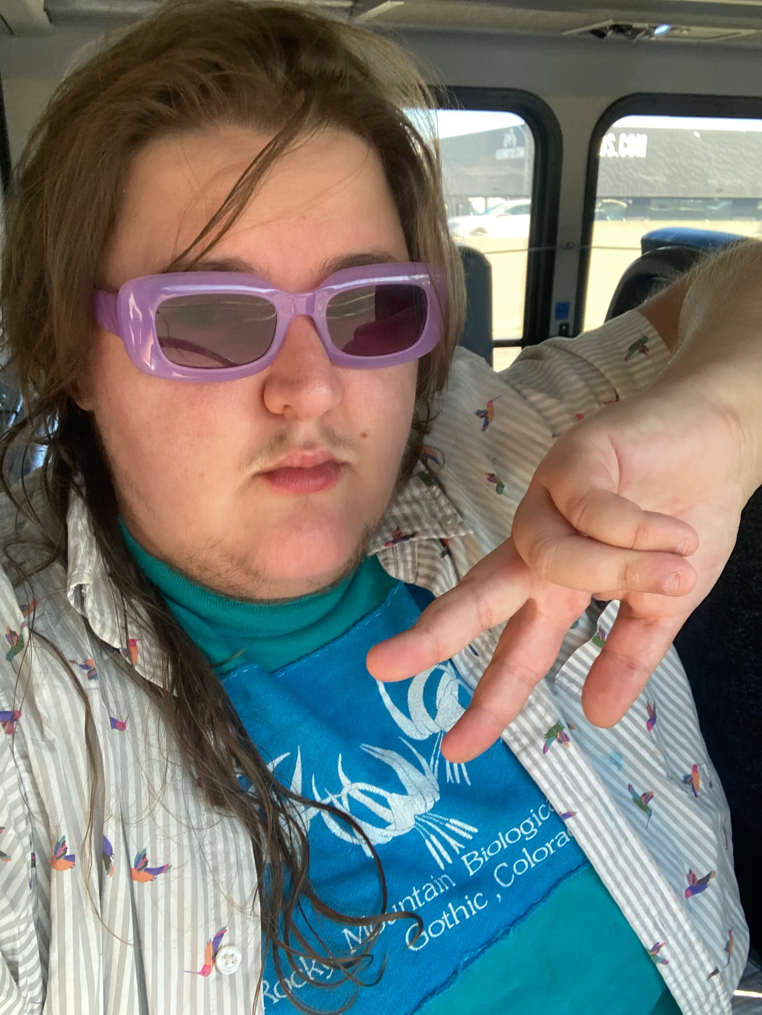white tboy in purple sunglasses making a peace sign inside a bus 