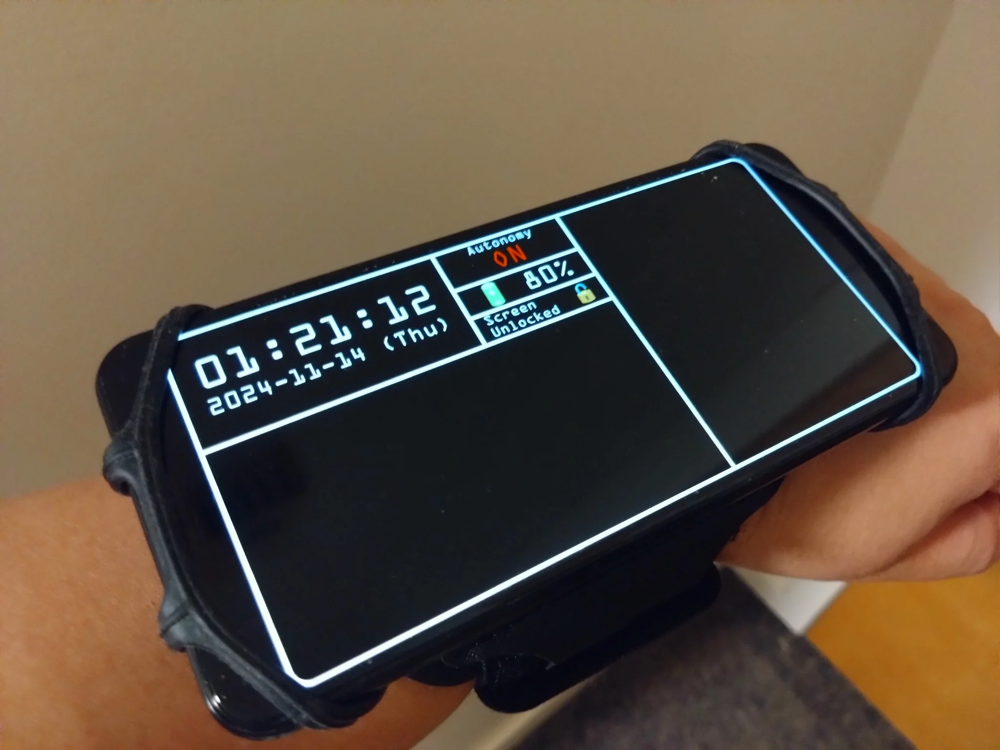 a pixel 3a (black phone) strapped to a rubber... holding thing that slots into a wrist strap.

on the phone's screen is the current time and date, the phone's battery percentage, a screen lock toggle and an autonomy toggle.