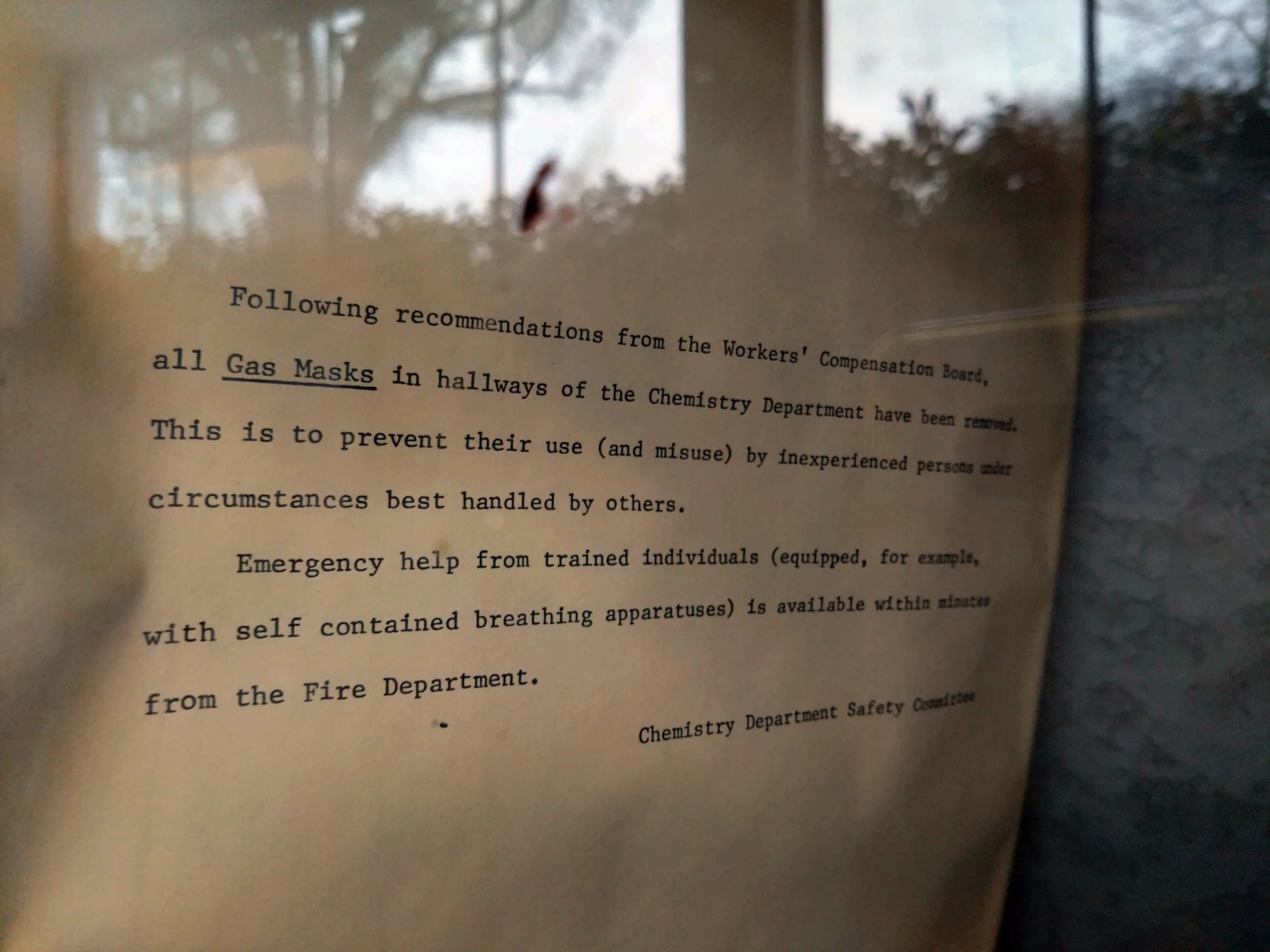 A typewritten message in a glass cabinet that says:

Following recommendations from the Workers' Compensation Board, all **Gas Masks** in hallways of the Chemistry Department have been removed. This is to prevent their use (and misuse) by inexperienced persons under circumstances best handled by others.

Emergency help from trained individuals (equipped, for example, with self contained breathing apparatuses)nis available within minutes from the Fire Department.

Chemistry Department Safety Committee