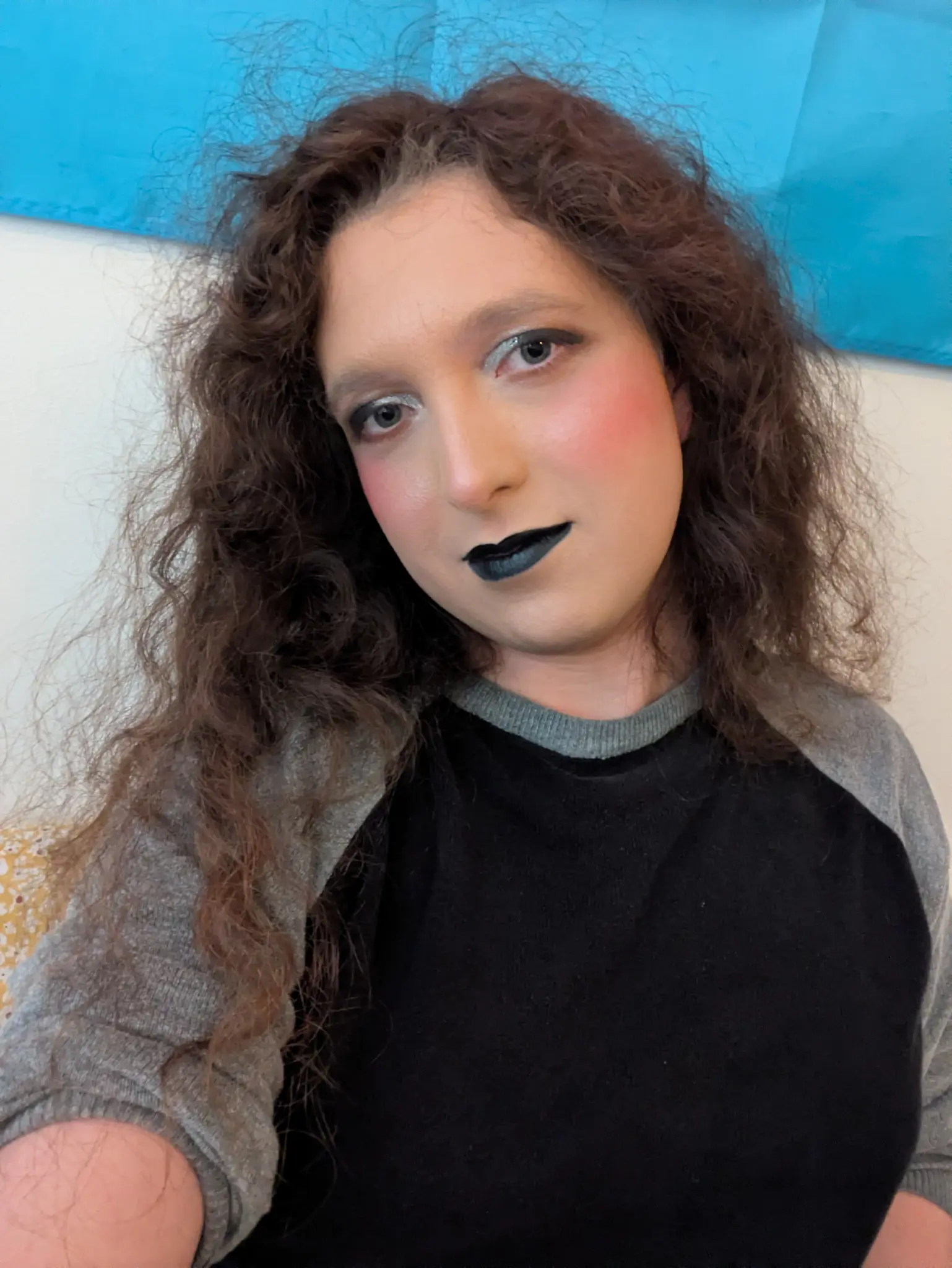 pale transfem wears goth makeup consisting of black and silver eyeshadow and black lipstick.