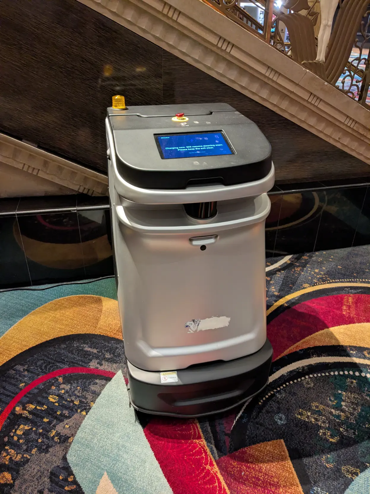 A carpet cleaning robot in it's charging bay. It's tall and rectangular with a white base and a black top