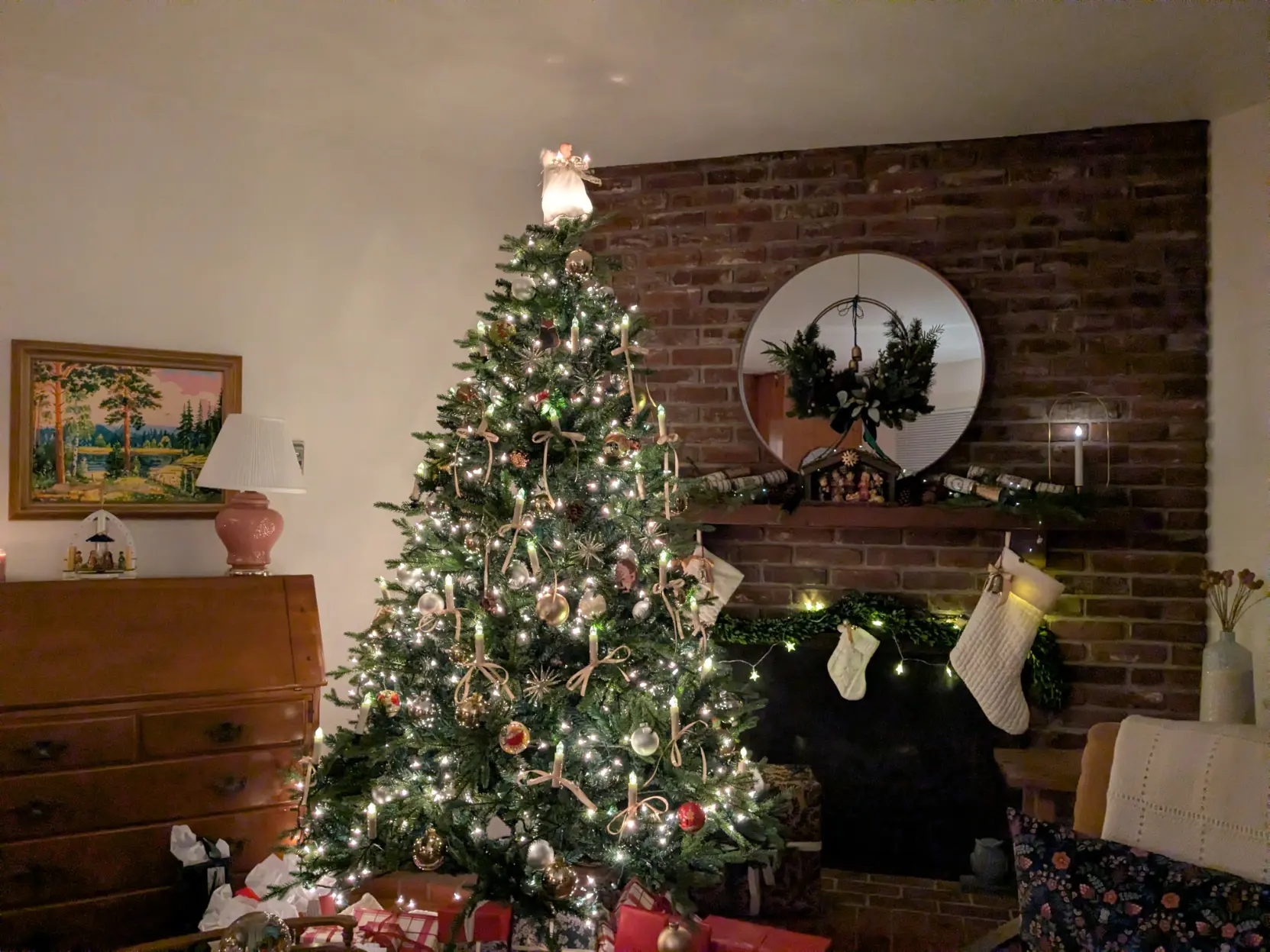 A Christmas tree with and angel and ornaments, a mantle and fireplace with garland, and stocking